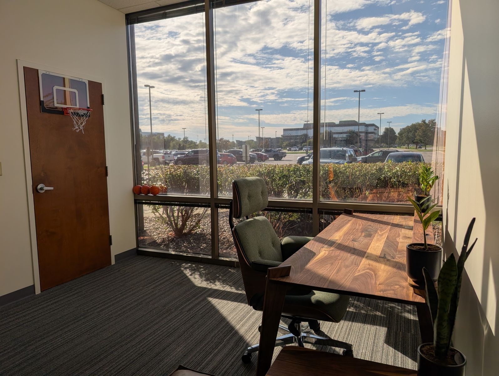 A walnut desk and green chair beside a large window in the office
